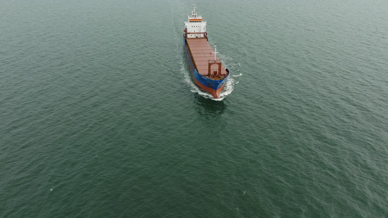 vista aérea de un gran buque de carga azul que sale del puerto de liepaja, puente de karosta, día ligeramente nublado, mar báltico tranquilo, tiro de avión no tripulado avanzando, inclinado hacia abajo