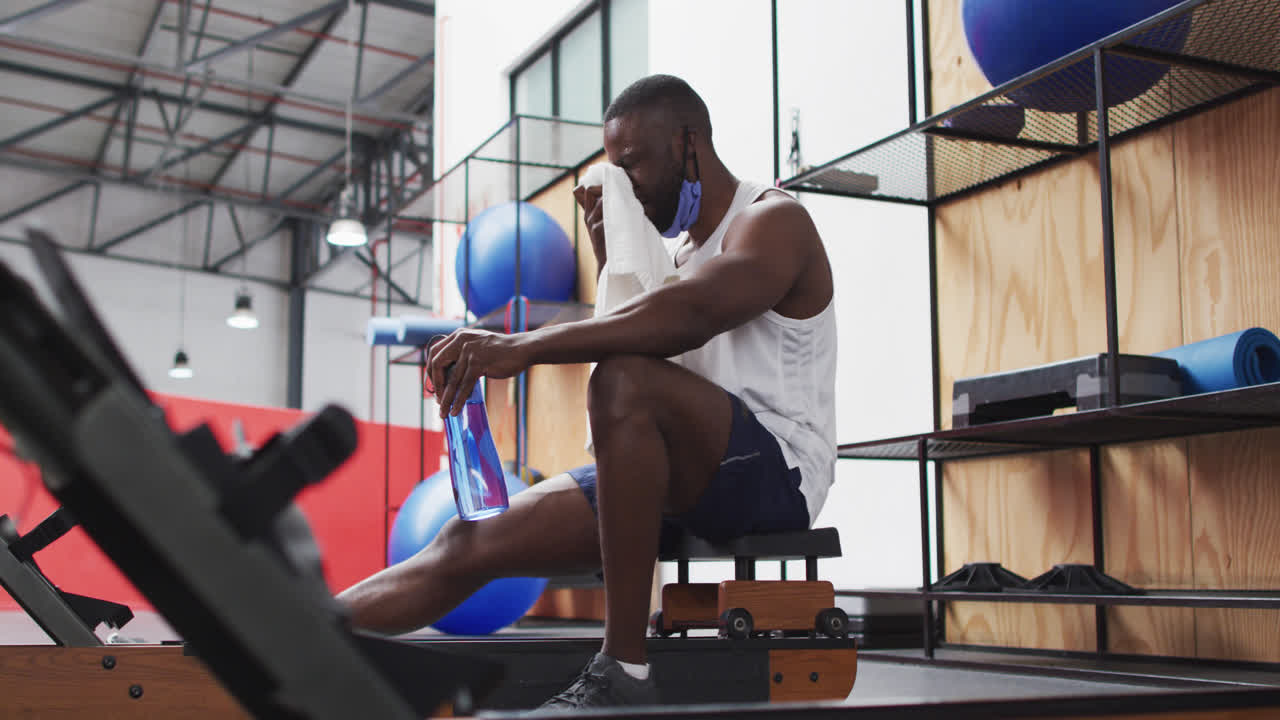 African american man wearing lowered face mask exercising at gym