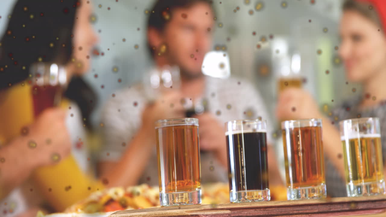 Animation of dark spots against close up of four shot glasses on bar table