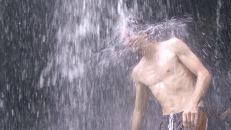 young man with long hair standing down a waterfall in comoros islands and shaking his head, moheli, slow motion