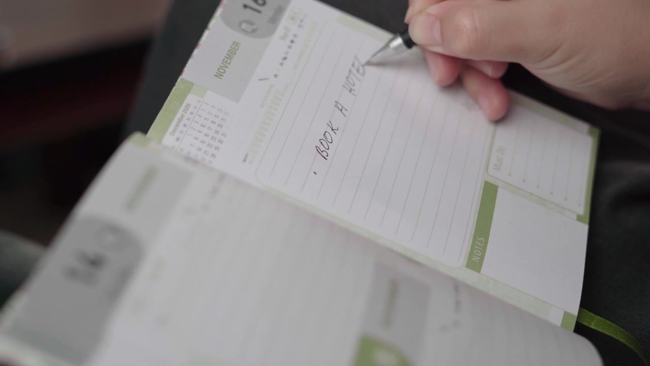 Una donna scrive un promemoria per la prenotazione di un hotel in un'agenda settimanale, organizzando i prossimi piani di alloggio per il viaggio.