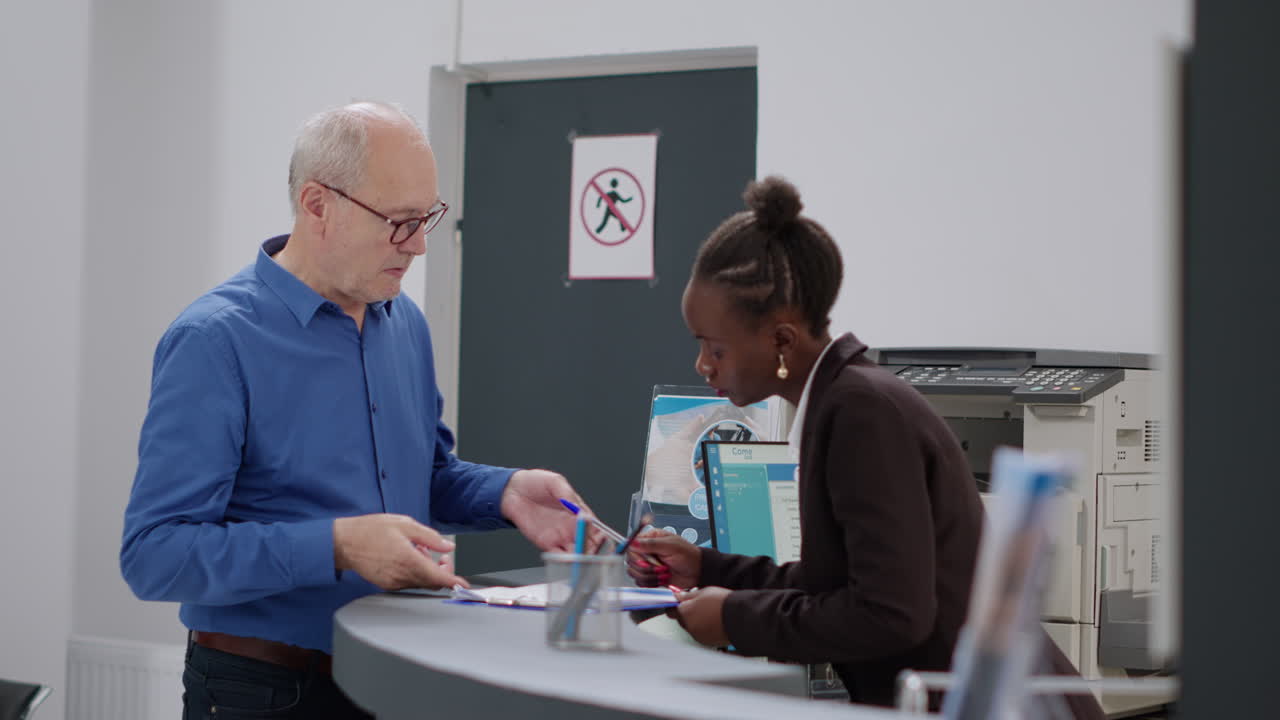 Man signing form at hospital reception with receptionist