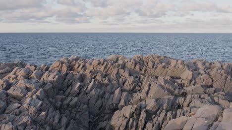 Blauer-Ewiger-Ozeanhorizont-Mit-Erstaunlichem-Felsigem-Kap-Im-Vordergrund-Bei-Sonnenuntergang