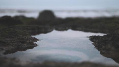 rockpool reflection shows cloudy sky rack-focus waves lapping at shoreline