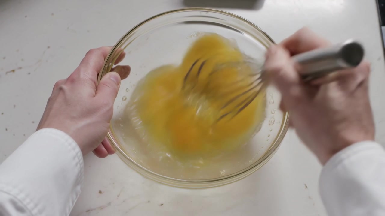 Whisking hands in longsleeve holding bowl with three eggs on counter, mixing for cooking with whisk