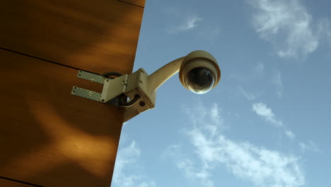 a security camera mounted on a rust-colored wall against a backdrop of blue sky