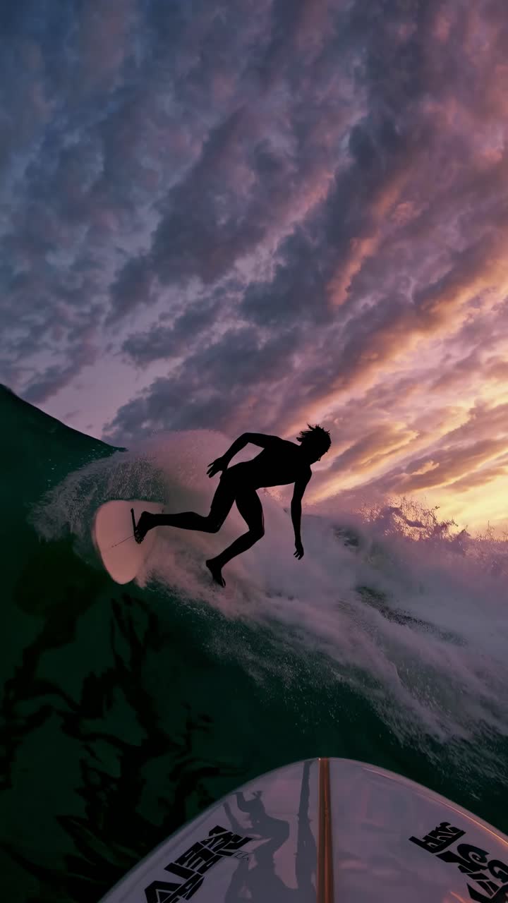 Ripresa video dinamica dal basso di un surfista che cavalca le onde al tramonto, catturando cieli vibranti