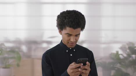 Retrato-De-Un-Joven-De-Raza-Mixta-Que-Busca-Mensajes-De-Texto-Enfocados-Navegando-Usando-Redes-De-Tecnología-Móvil-De-Teléfonos-Inteligentes-En-El-Fondo-Del-Espacio-De-Trabajo-De-Oficina