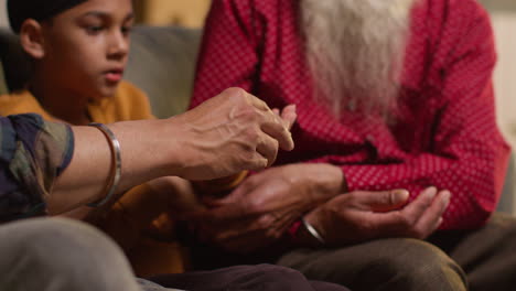 primer plano de una familia sikh masculina de varias generaciones usando y discutiendo brazaletes o pulseras tradicionales de plata sentados en el sofá en casa 4