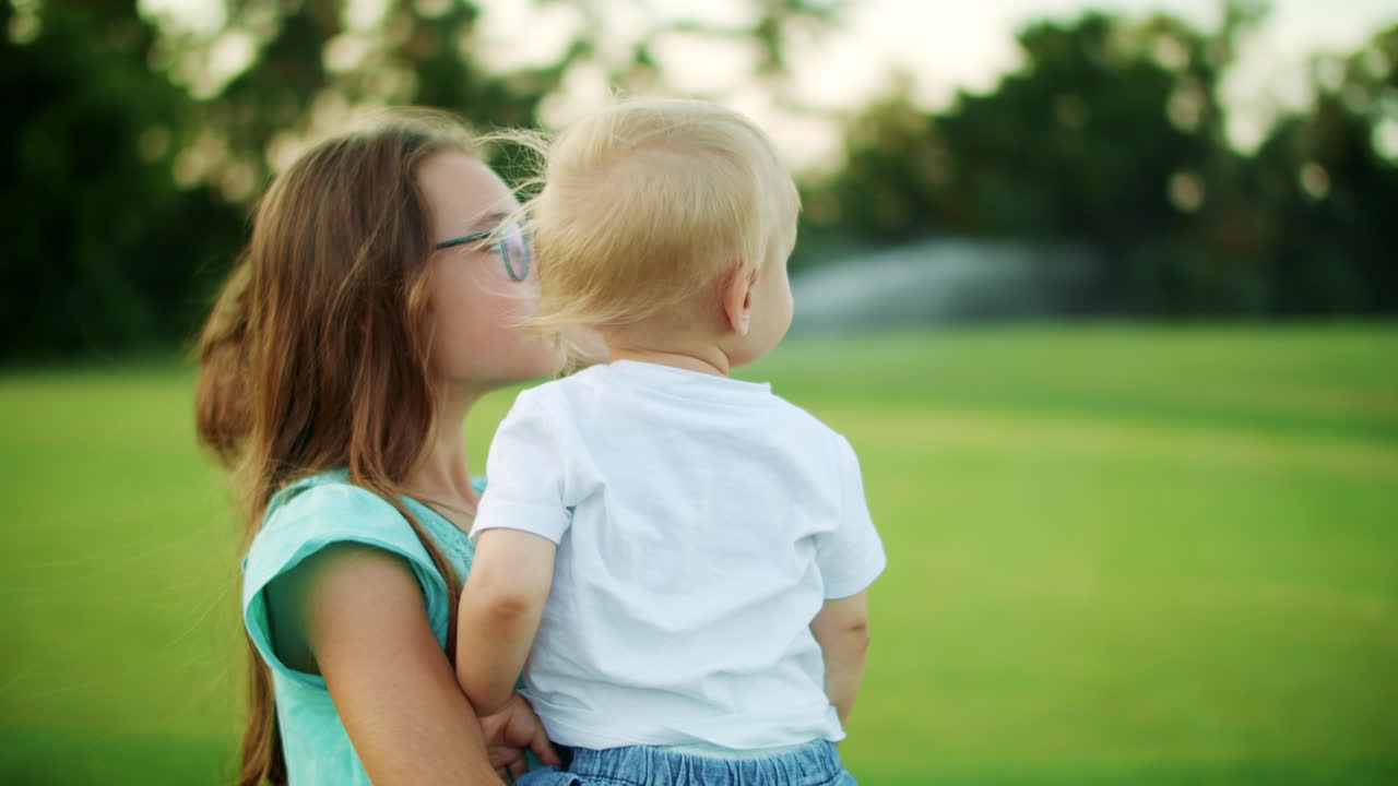 Bambini adorabili in piedi in un campo verde. Sorella maggiore che tiene in braccio il fratello.