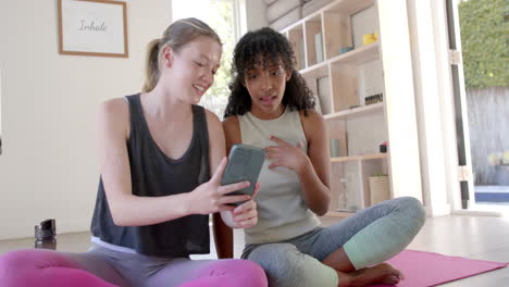 mujeres felices y diversas sentadas en esteras de yoga y usando teléfonos inteligentes, en cámara lenta