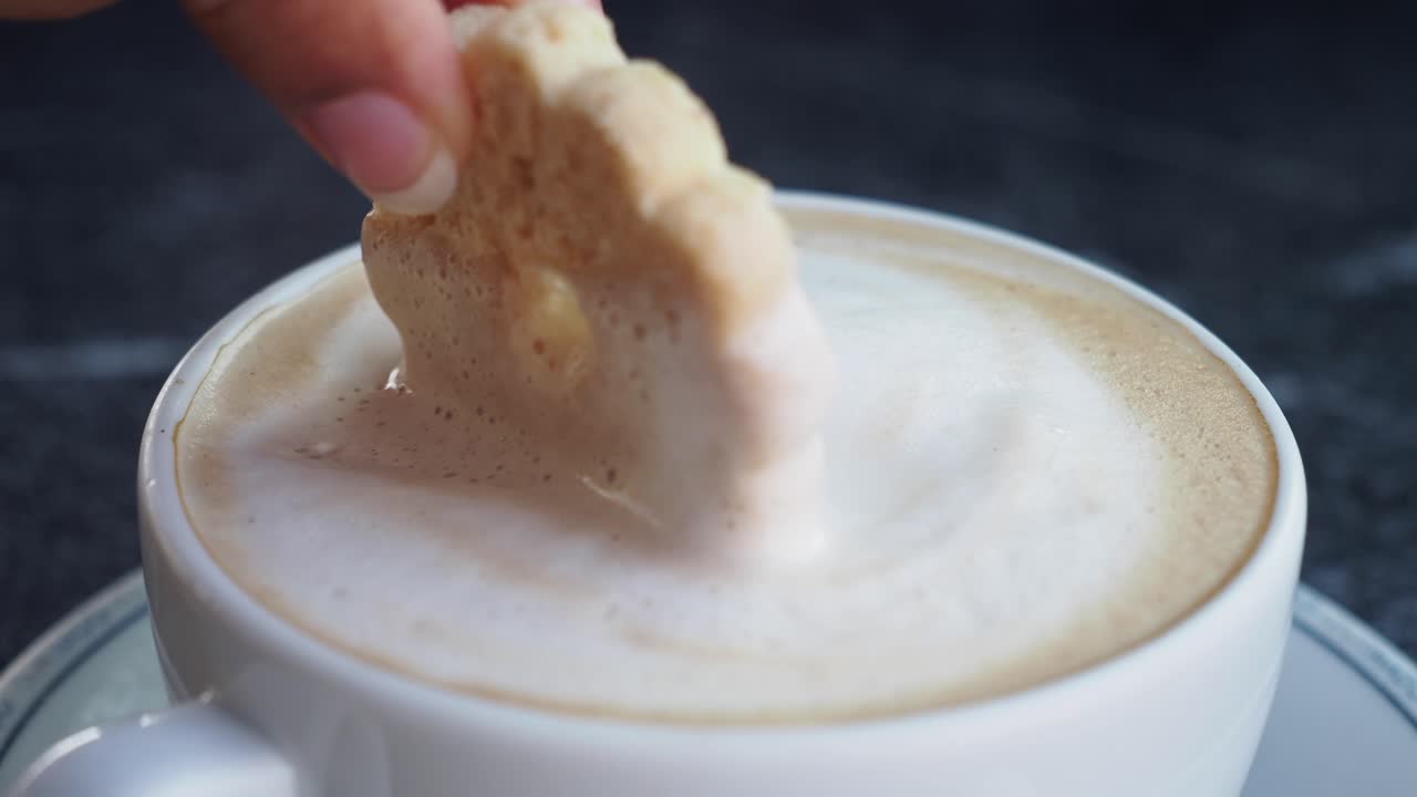 Hand dipping cookie into cappuccino