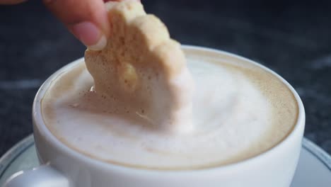hand dipping cookie into cappuccino
