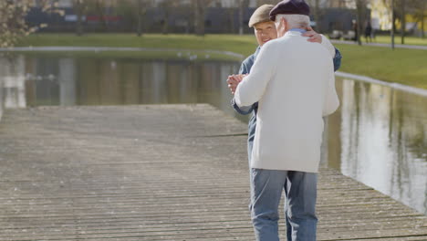 Pareja-De-Ancianos-Bailando-En-El-Muelle-En-El-Parque-De-La-Ciudad-En-Un-Cálido-Día-De-Otoño-Con-Edificios-De-Varios-Pisos-En-El-Fondo-1