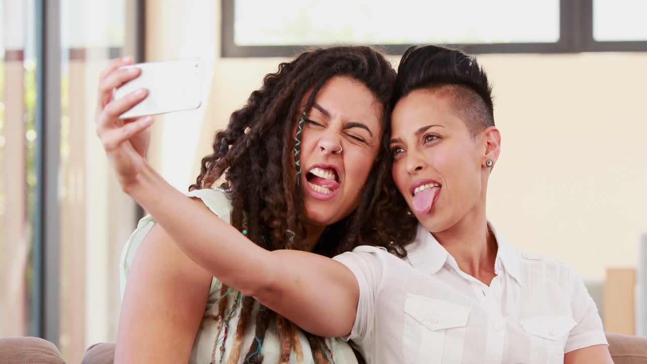 Coppia lesbica sorridente sul divano che si scatta un selfie