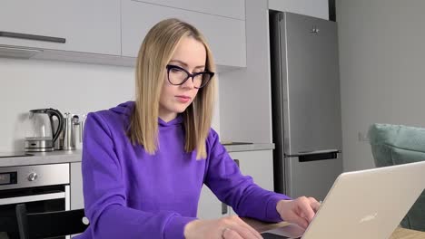 mujer adulta joven pensativa con gafas trabaja estudia en la cocina usando portátil. trabajo desde el concepto de casa
