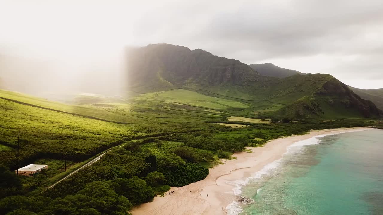 Smuk 4K droneoptagelse panorerende over kystlinjen ved Makua Beach på vestsiden af Oahu med morgensolens stråler, der falder over de grønne bjerge