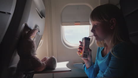 the child in the cabin of the plane - drinking juice from the tube with her flying toy - a hare 4k v