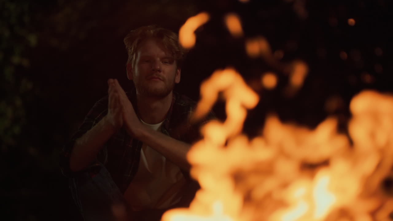 primer plano campista relajado fuego cálido en la actividad de campamento de noche. joven mirar fuego de campamento
