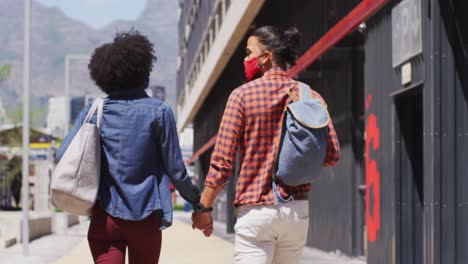 diverse couple wearing face masks walking and holding hands