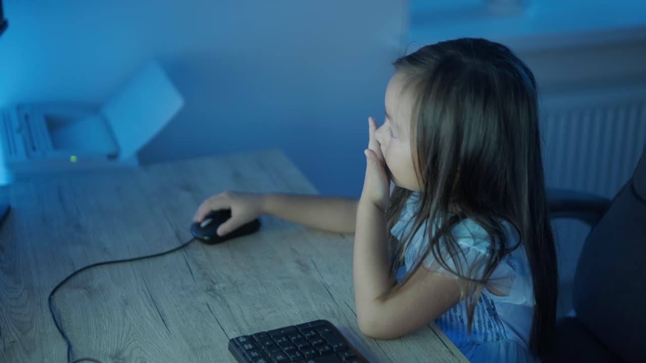어린 소녀가 컴퓨터 앞에 앉아서 강한 감정을 표시합니다. 이 장면은 편안한 실내 환경에서 펼쳐지는 매력적인 순간 동안 그녀의 표현적 반응을 포착합니다.