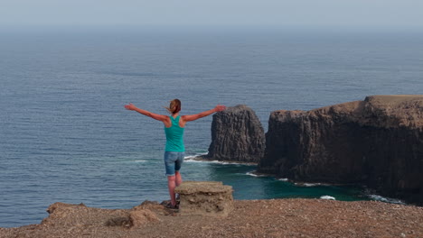 female traveler standing on rocky volcanic cliff, overlooking expansive atlantic ocean coastline with panoramic gran canaria landscape under bright sunlight