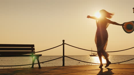 the woman is happily spinning on the pier holding a hat in her hand the sunrise meets happy woman on