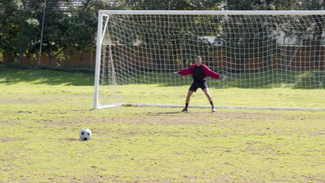 Playing soccer, boy scoring goal while goalkeeper diving to save ball