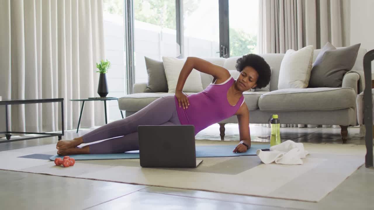 Happy african american wearing sportswear, exercising, using laptop