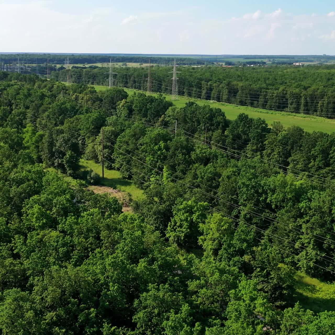 High voltage steel power pylons. Transmission lines in summer day. Electric tower lines among green nature at daylight. Aerial view.