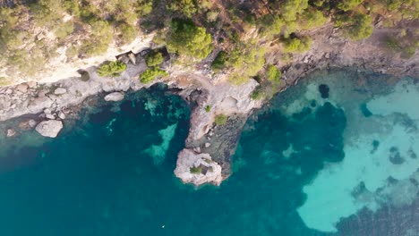 Aerial-top-down-ascend-over-limestone-cliff-and-turquoise-lagoon,-Mallorca