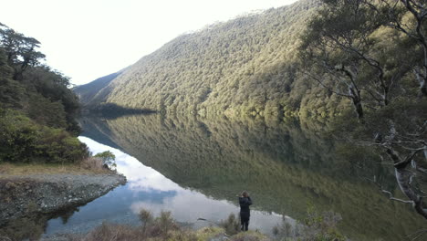 girl walking down to a calm lake with a reflection of the lush green mountains surrounding it