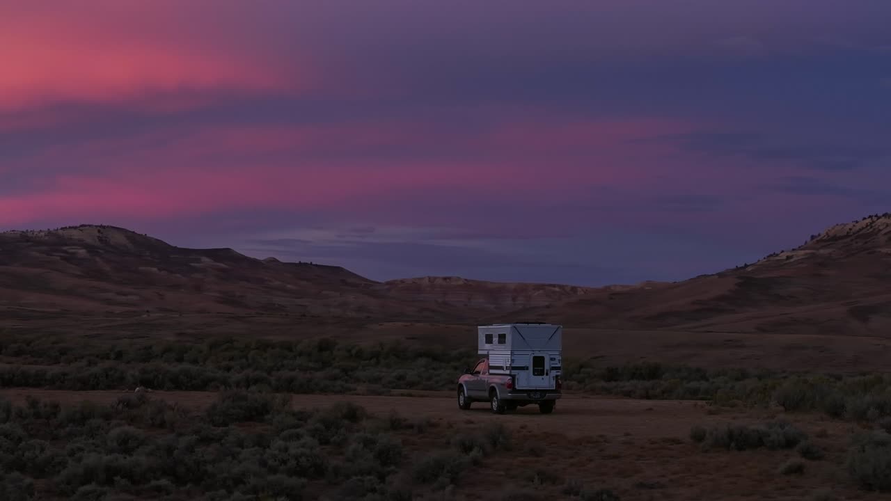 Trailer estacionado em planície aberta de artemísia sob o céu crepuscular rosa e colinas desérticas