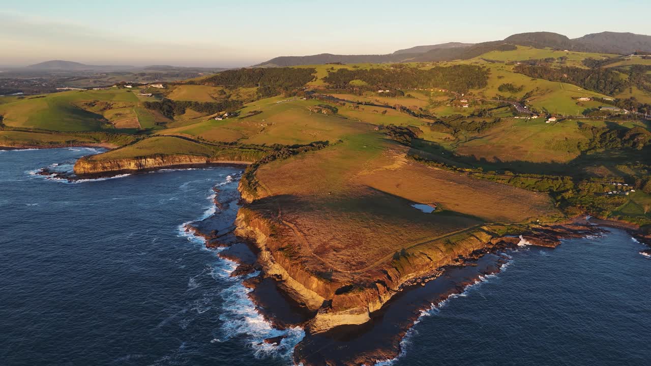 High angle drone orbit of dramatic coastal cliffs in Kiama meeting deep blue ocean waters