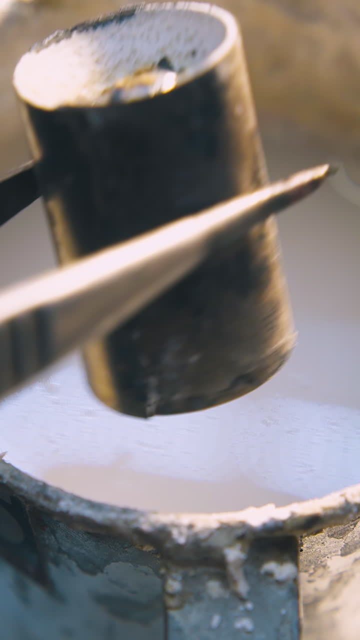 CU: skilled worker puts cylindrical metal bar into high container with white liquid on table in production workshop closeup