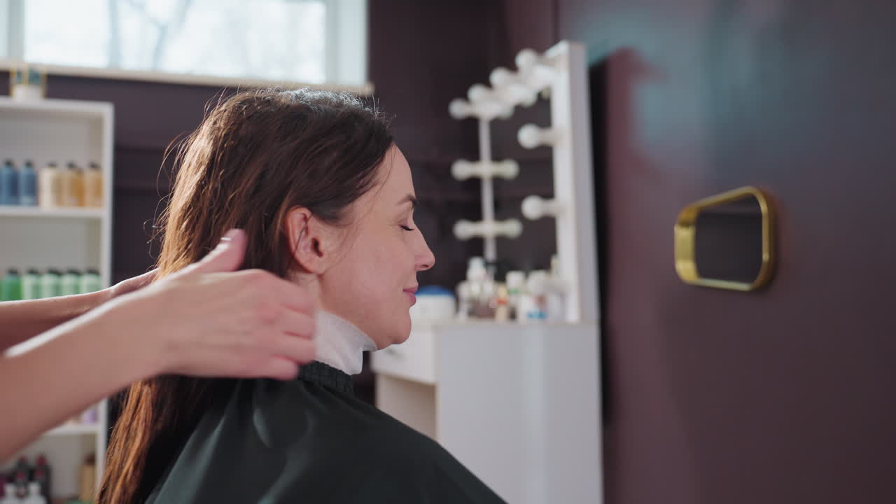 스타일리스트가 머리를 정돈하고, 우아한 헤어스타일을 준비 및 섹션으로 나누고, 스타일리스트가 능숙하게 머리를 섹션으로 나누어 세련된 올림머리를 만들고, 스타일리스트가 차분한 분위기 속에서 머리카락을 깔끔하게 정리합니다.