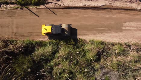toma aérea de arriba hacia abajo del vehículo de rodillos que nivela el camino arenoso a la luz del sol