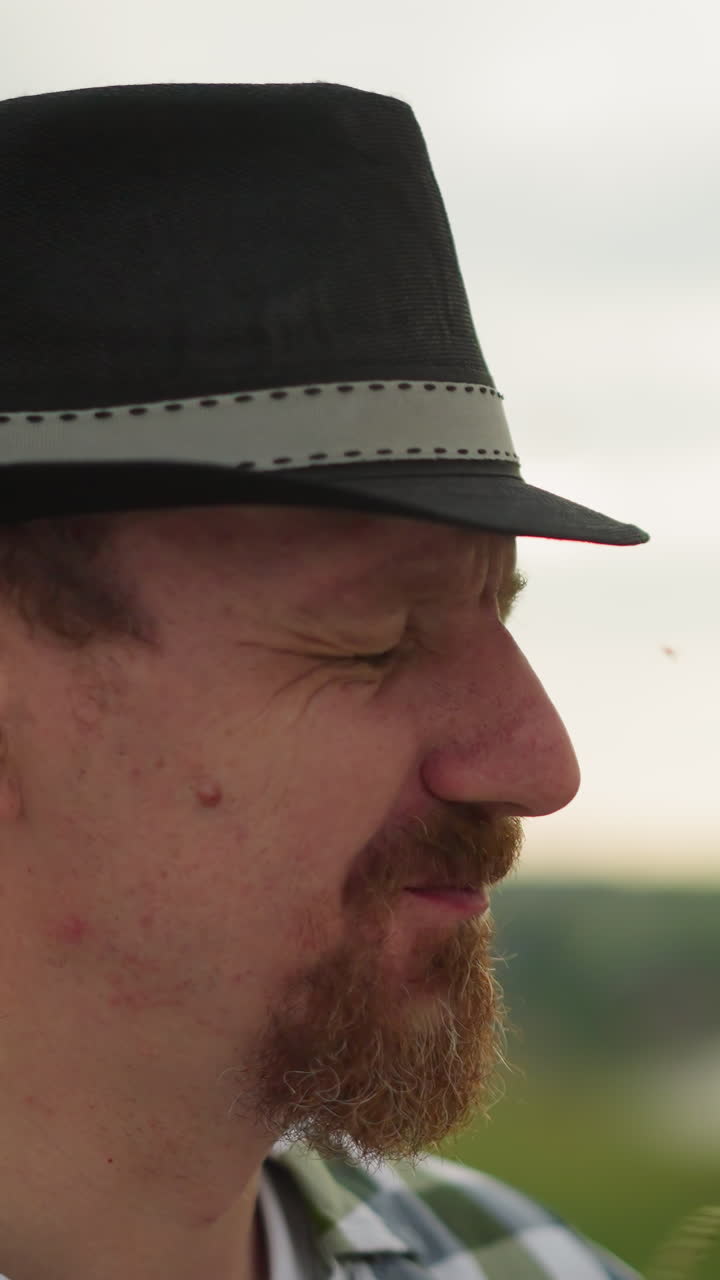 모자를 입은 남자의 클로즈업, 여성의 손이 잔디 어리로 그의 코를 만질 때 부드럽게 미소 짓고, 배경은 흐릿합니다.