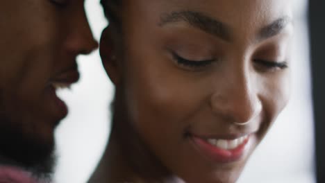 Close-up-of-happy-african-american-couple-standing-at-window-and-hugging