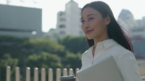 young asian businesswoman walking in city with laptop and coffee