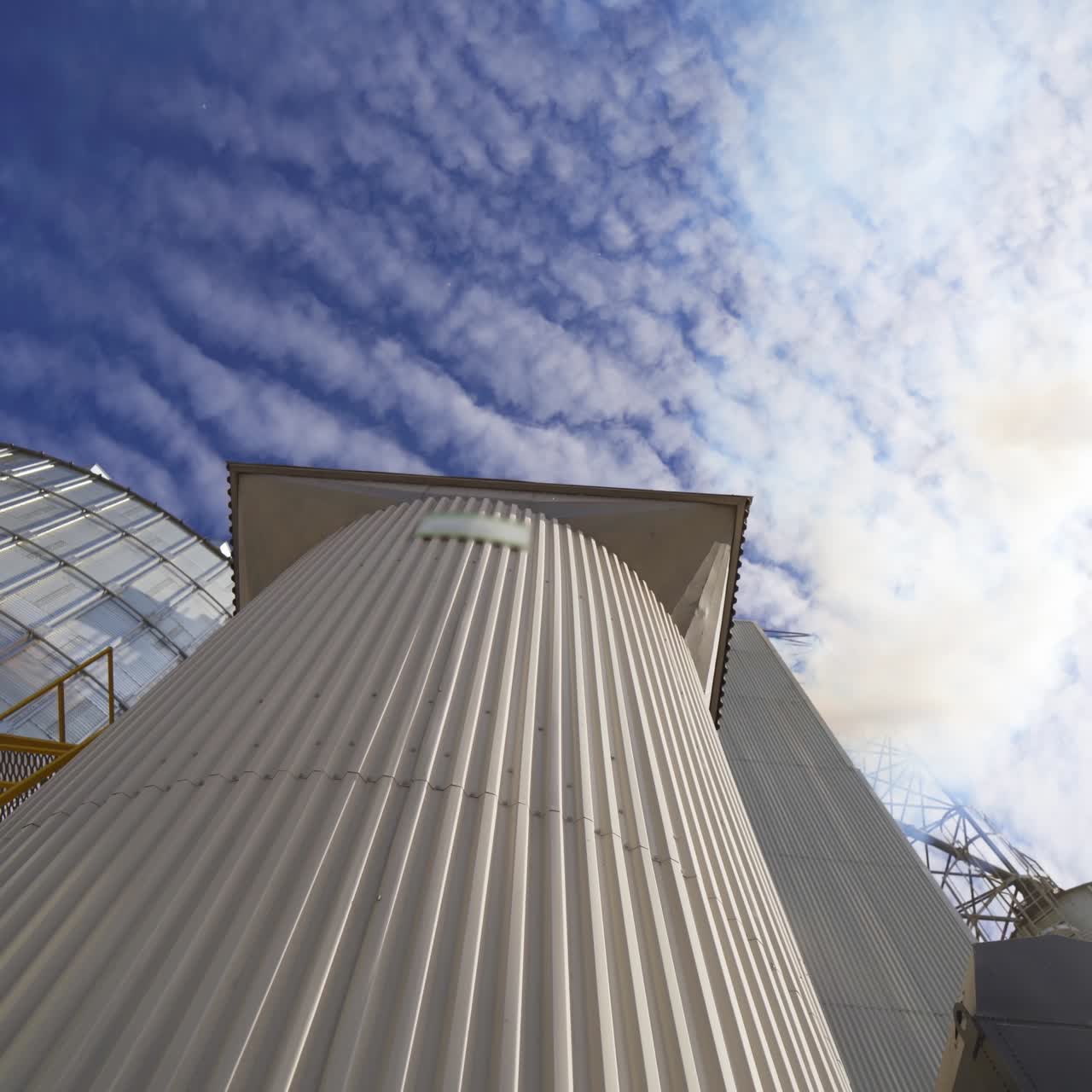 Metal grain elevator on sky background. Large granary for storing cereals. Thick smoke releasing into the air from industrial plant. Pollution. View from below