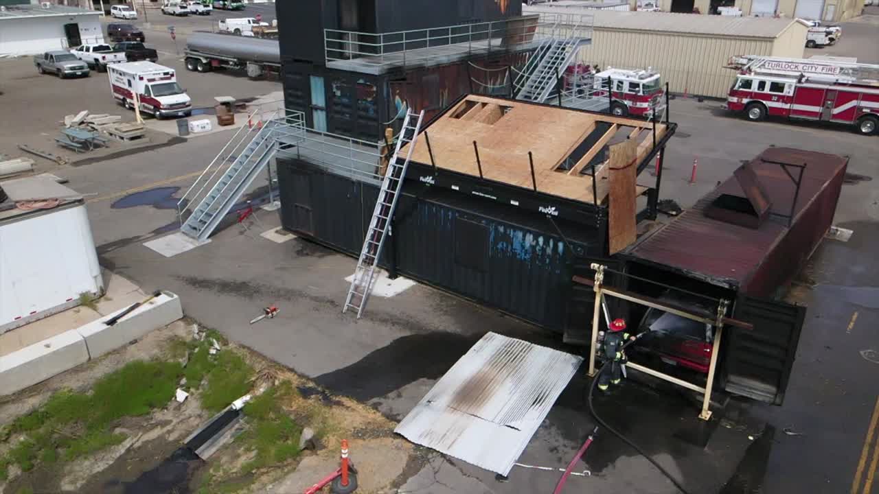 slow motion drone aerial footage of two firefighters in full gear helmet jacket extinguishing fire in truck in metal container panning out on gushing water and hose emergency services