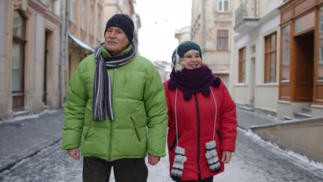 pareja de ancianos turistas hombre mujer familia caminando, hablando, gesticulando en invierno calle nevada de la ciudad