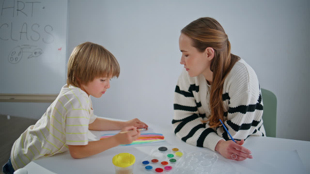 Art tutor helping pupil with palette in workshop closeup. Lady teaching kid
