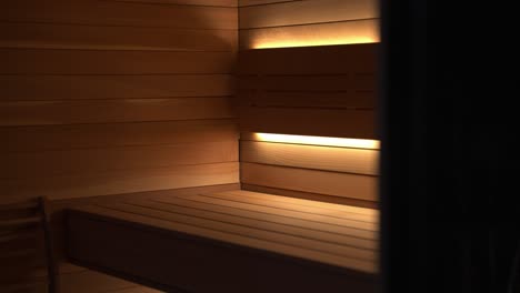 close up reveal of wooden hand crafted seat bench inside a luxury sauna at night with an orange under glow light creating ambience