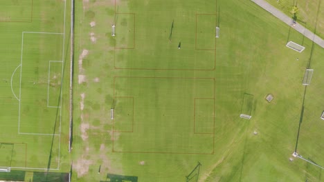 aerial footage captures a soccer field with people walking, under clear daylight, showcasing the expansive green landscape