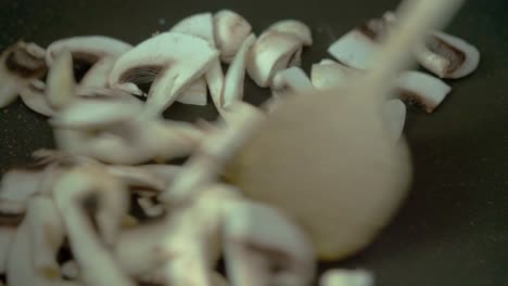 young female adding mushrooms in frying pan then stir frying them