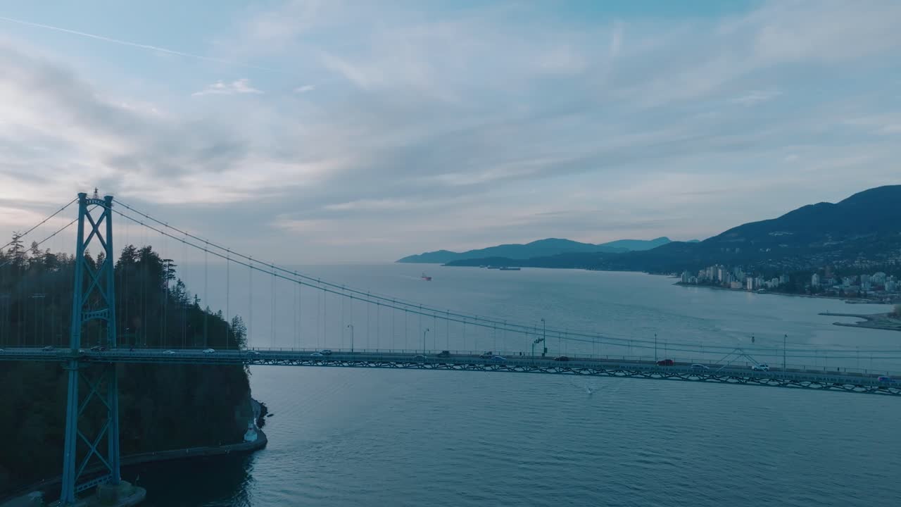 Riprese aeree con drone che volano intorno al Lions Gate Bridge a Vancouver, Columbia Britannica, che si concludono con un tramonto invernale cinematografico, una calda luce dorata e viste panoramiche della città costiera
