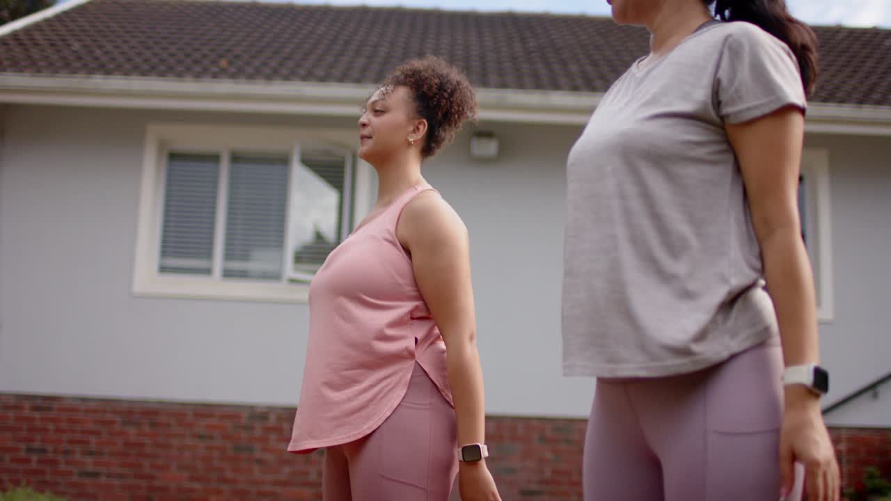To kvinder i leggings, der laver squat med træningselastik på forplænen, med loop-elastikker og smartwatches