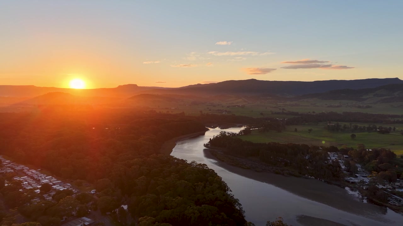 Gerroa, Austrália, estuário de rio ao pôr do sol, água calma do rio, reflexos da hora dourada, céu rosa e laranja, paisagem costeira, natureza tranquila, cinematográfico, luz do crepúsculo, área residencial próxima, minimalista.